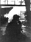 Schwarz-weiß Foto, Frau mit Hut sitzt auf einem Koffer am Bahnhof, Gegenlicht